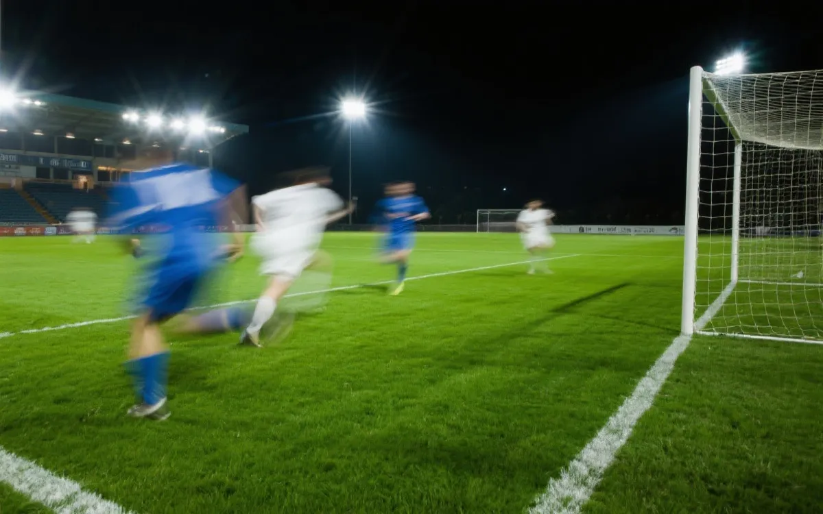 夜间灯光下的决赛球场，草皮反光与球员冲刺形成强烈速度感，电影感体育摄影